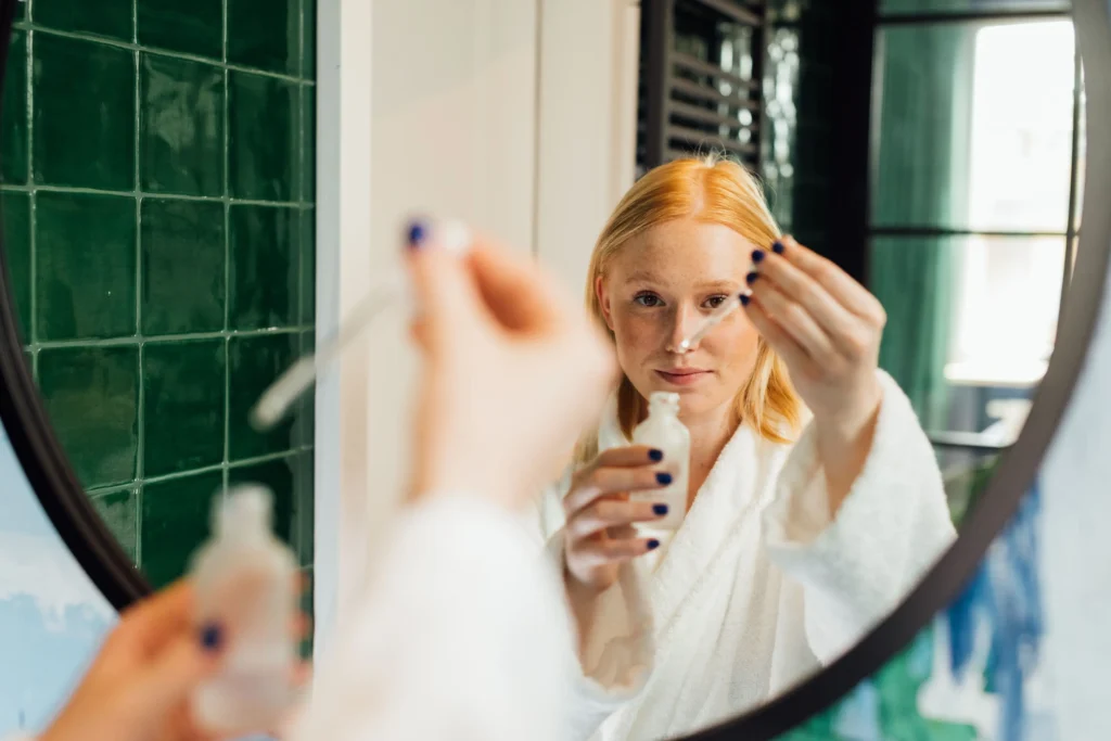 Woman following a daily skincare routine using cleanser, serum, moisturizer, and sunscreen for healthy-looking skin.